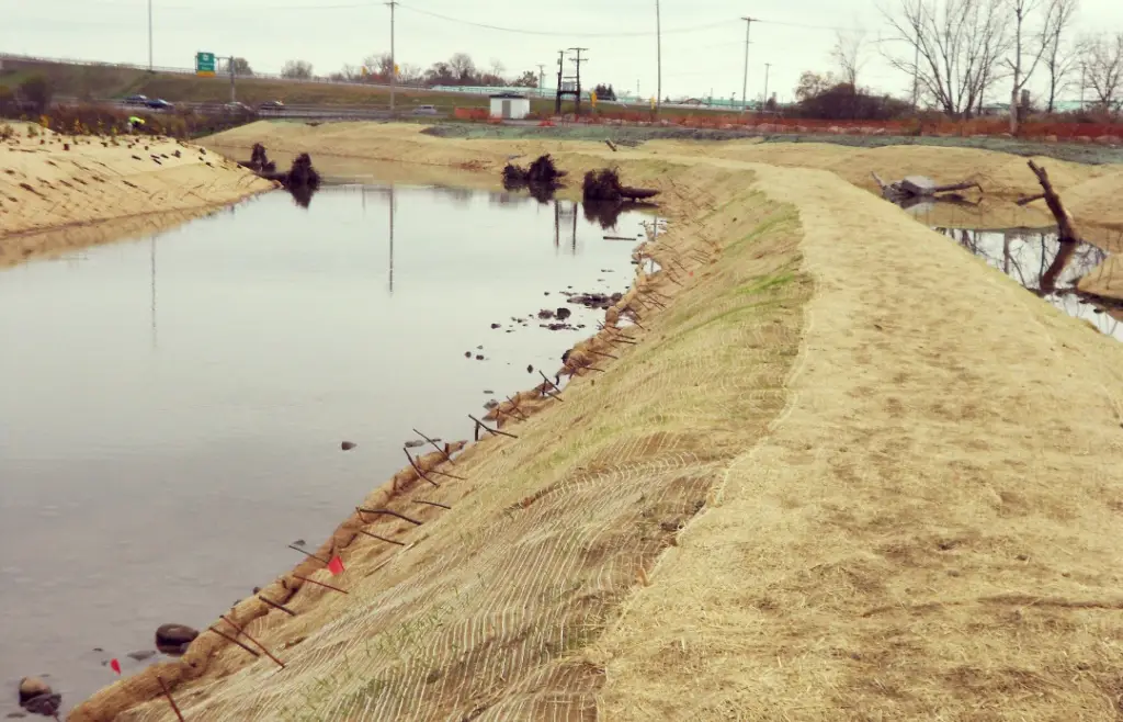 Biodegradable erosion control blankets installed along a waterway to stabilize soil and prevent sediment runoff, showcasing sustainable landscaping techniques for environmental protection